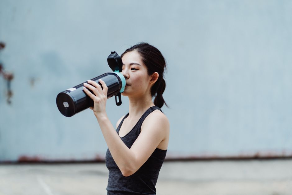 A young Asian woman drinks from a bottle while exercising outdoors, staying hydrated during her fitness routine.