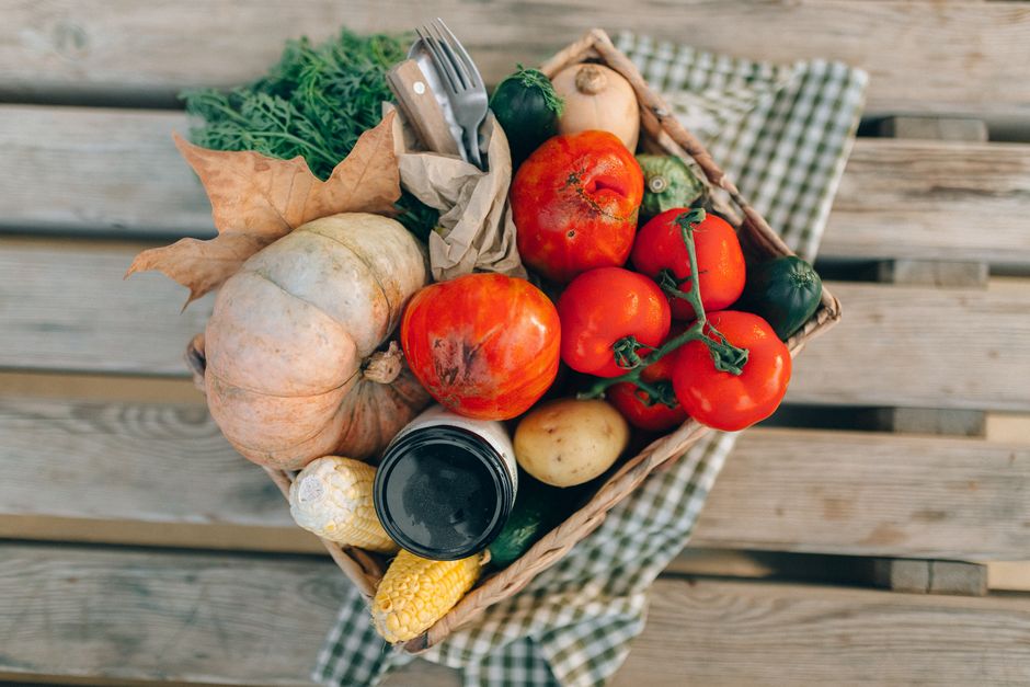 A top-down view of a basket filled with fresh vegetables and produce, placed on a wooden table.