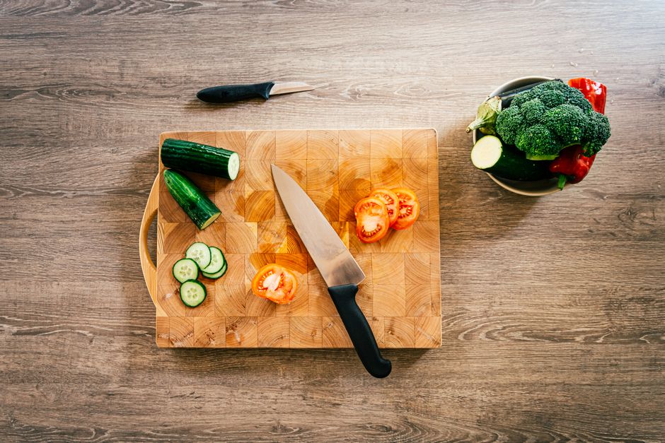 Sliced cucumbers and tomatoes on a wooden cutting board with a knife.