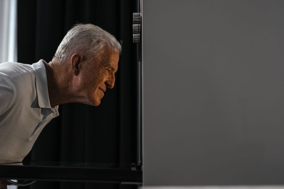 Senior man peeking into oven with excitement, showcasing curiosity and anticipation.