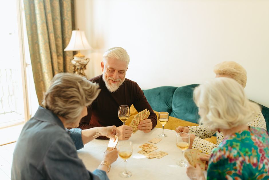 Group of elderly friends playing cards with wine indoors enjoying leisure time.