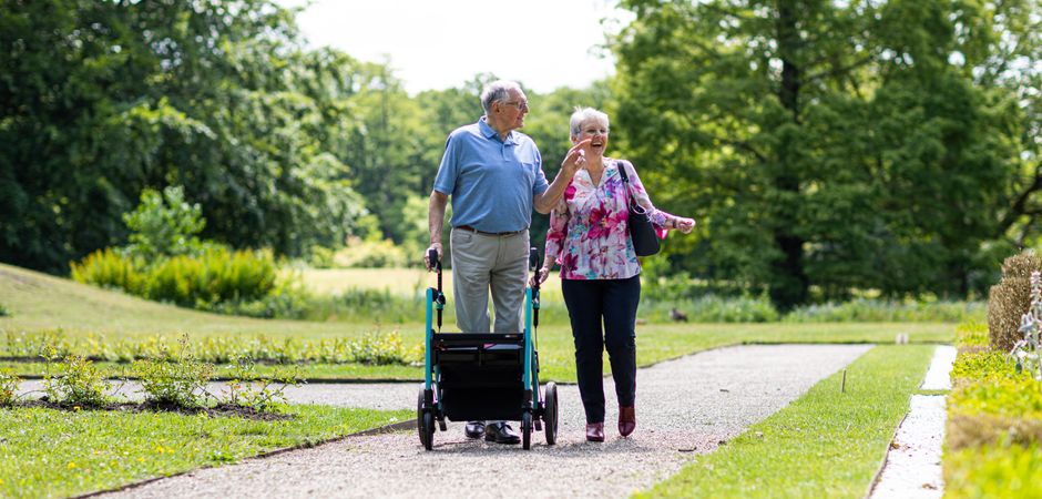 Senior couple walking in a park with a walker, enjoying a sunny day outdoors.