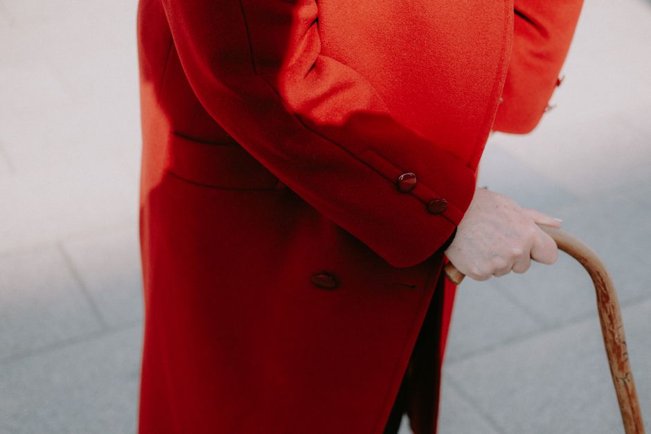An elderly person in a red coat holds a cane, reflecting elegance and style.