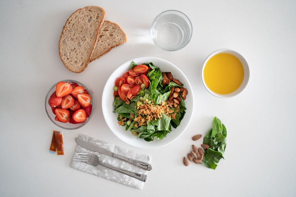 Top view of a healthy salad and fresh ingredients with bread and juice on a white surface.