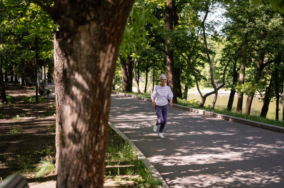 A senior woman jogging along a tree-lined path on a sunny day, embracing a healthy lifestyle.