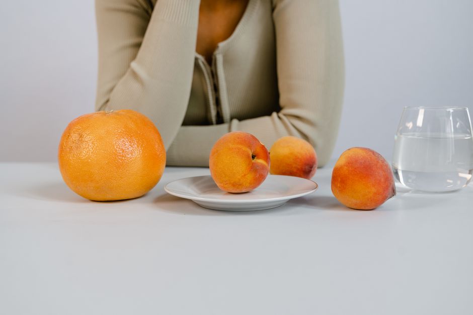 A close-up of fresh peaches and a grapefruit with a woman blurred in the background.