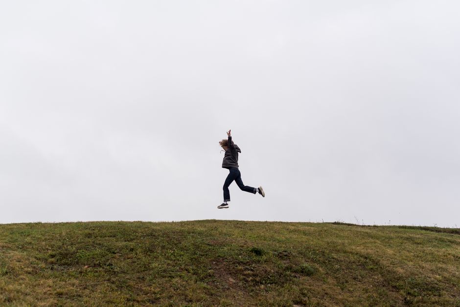 A person joyfully jumping on a grassy hill under a cloudy sky, depicting freedom and excitement.