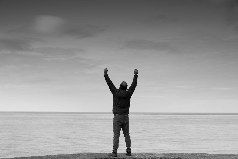 Black and white image of a person raising arms in celebration by the sea.