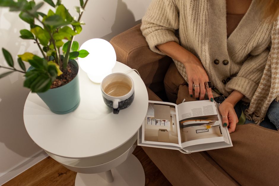 A warm, inviting scene of a person reading and enjoying coffee in an indoor setting with a plant beside them.