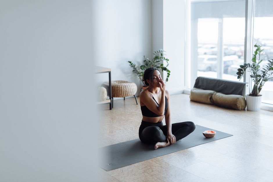 A woman meditating indoors on a yoga mat, promoting tranquil well-being.