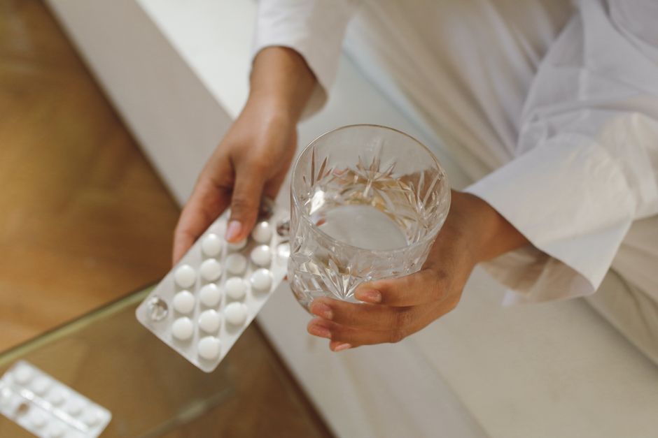 Close-up image of hands holding pills and a glass of water, ideal for health and wellness themes.