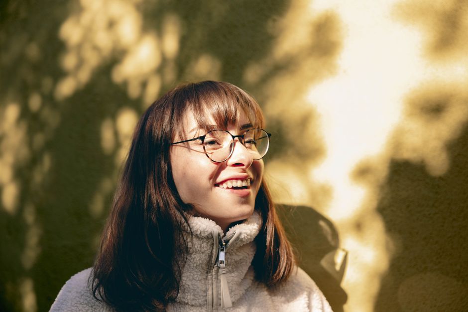 Portrait of a young woman with glasses enjoying sunlight outdoors, capturing a joyful moment.