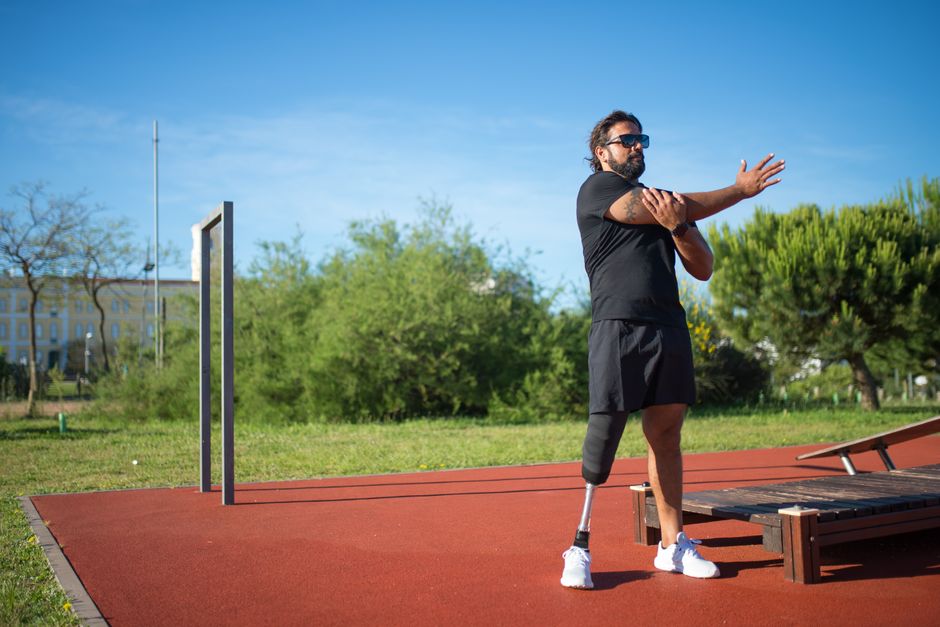 Man with prosthetic leg stretches outdoors in a sunny park, promoting fitness and inclusion.