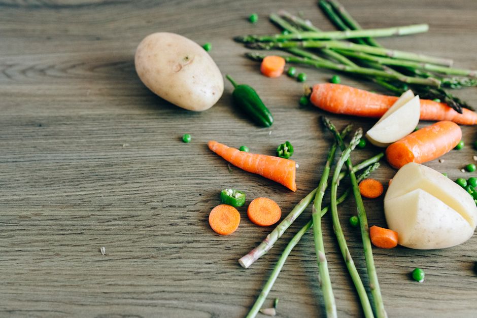 A variety of fresh organic vegetables including carrots, peas, and asparagus on a wooden surface.