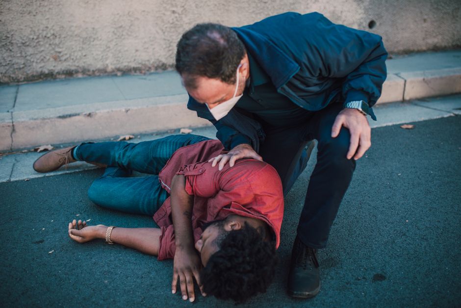 Paramedic aiding an injured man lying on the roadside, showcasing emergency care.