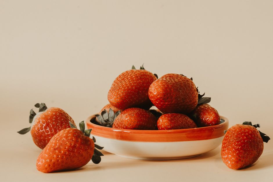 A stack of ripe, vibrant strawberries in a ceramic bowl against a neutral backdrop.