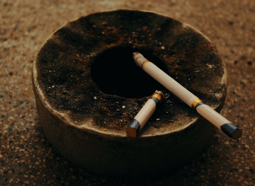 An antique ashtray with two burnt cigarettes on a textured surface, creating a moody atmosphere.
